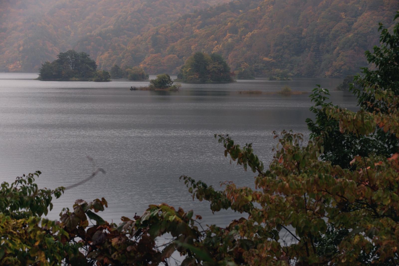 「秋元湖の薄明で照らされる紅葉と静かな湖面」の写真