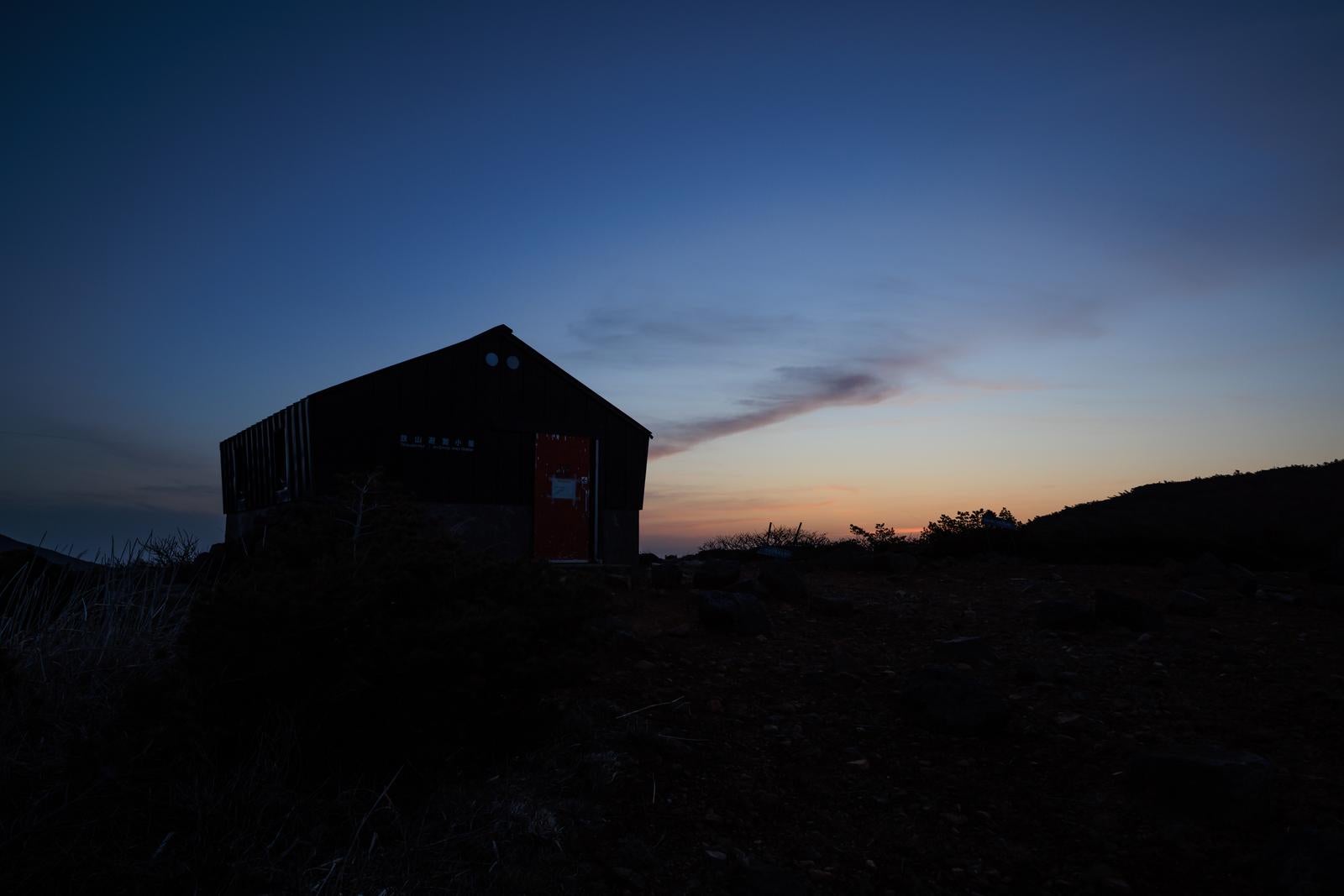 「薄明に浮かぶ鉄山避難小屋のシルエット」の写真