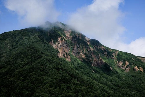 山肌と雲がかる磐梯山の写真