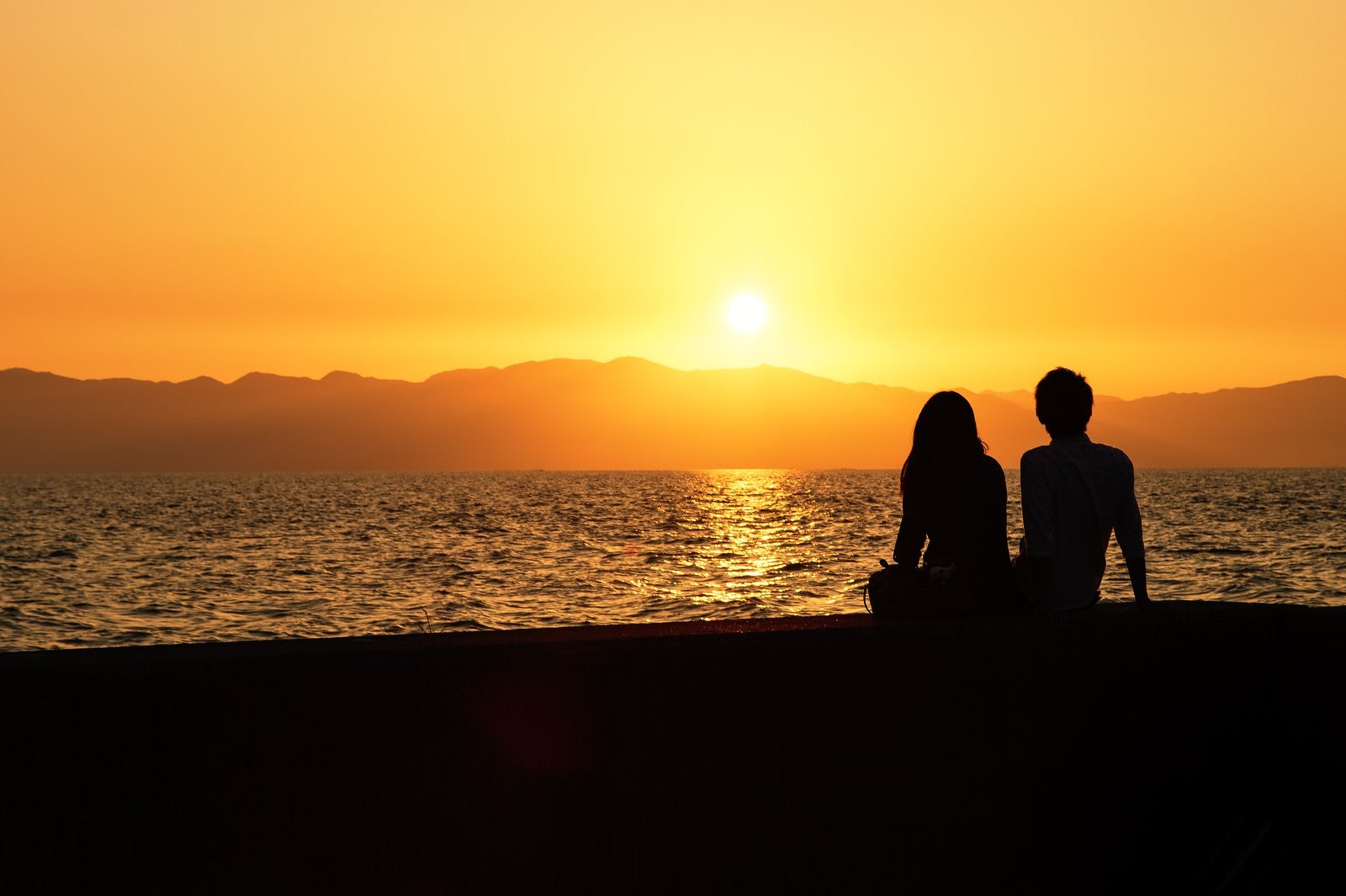 「海沿いの夕焼けとカップルのシルエット」の写真