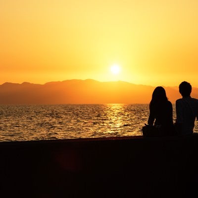 海沿いの夕焼けとカップルのシルエットの写真
