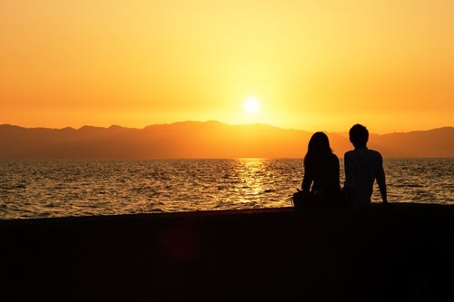 海沿いの夕焼けとカップルのシルエットの写真