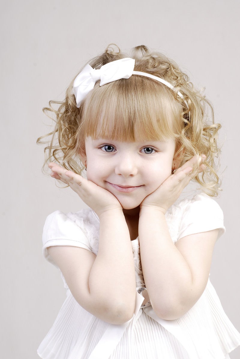 「白いドレスを着て可愛さアピールをするブロンドヘアの幼い女の子」の写真［モデル：モデルファクトリー］
