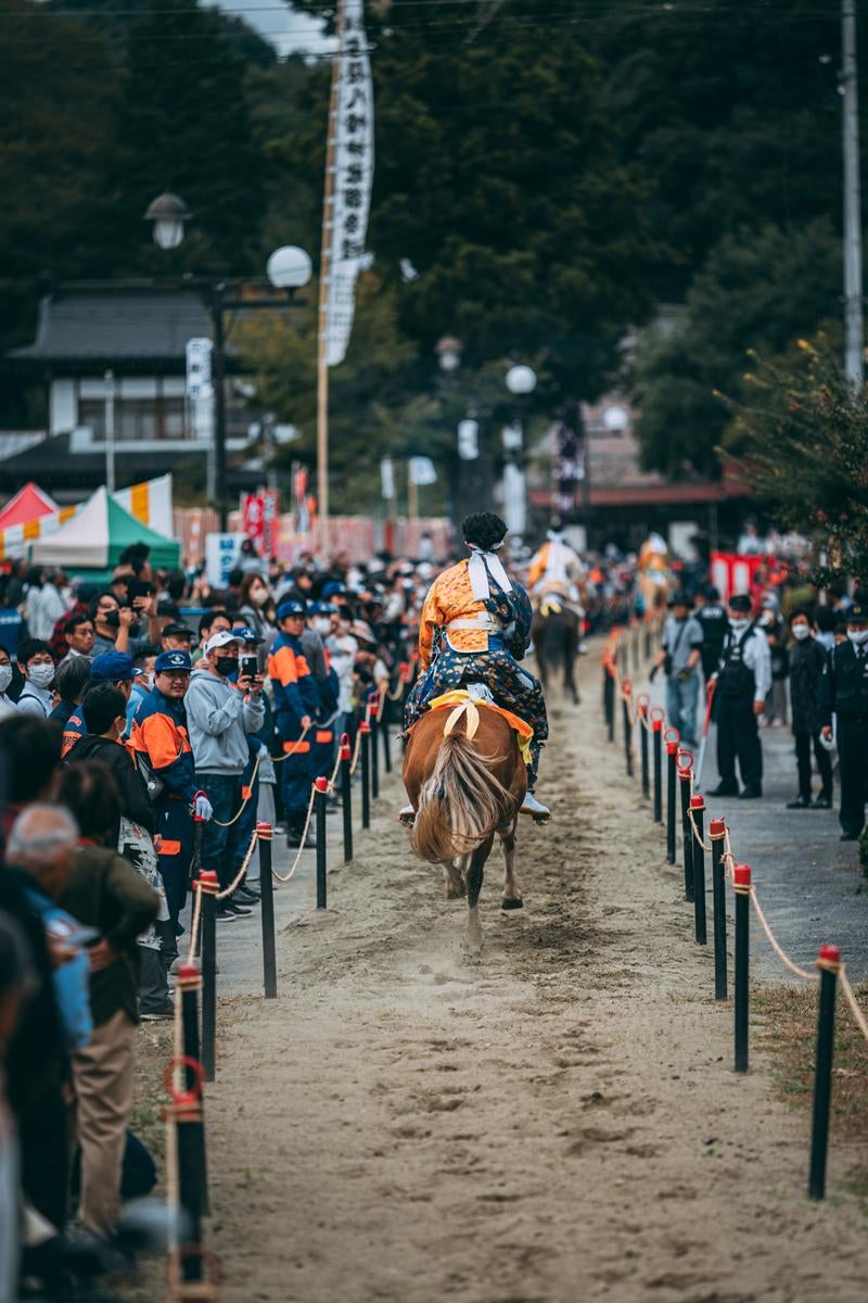 「流鏑馬を見守る観客の存在と走り抜ける騎馬の後ろ姿」の写真