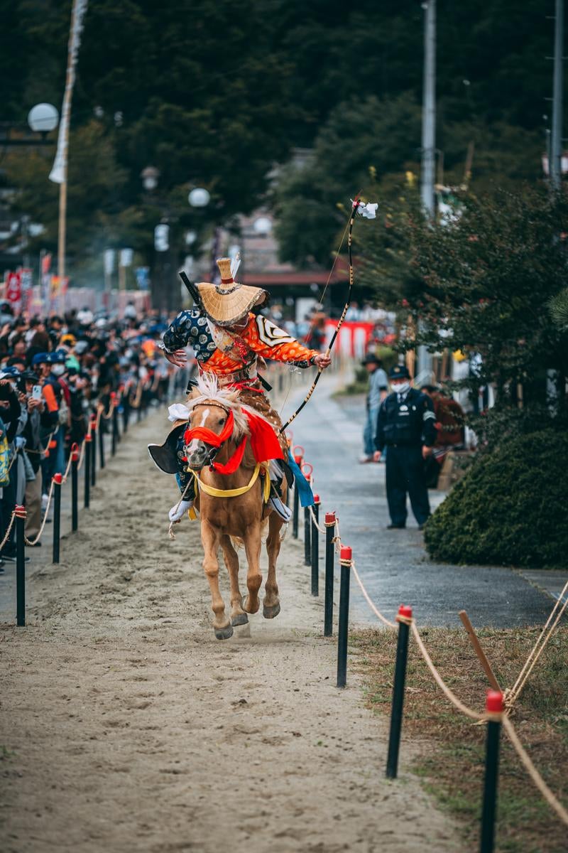 「古殿八幡神社で開催される流鏑馬の騎馬と騎手が駆け抜ける様子」の写真