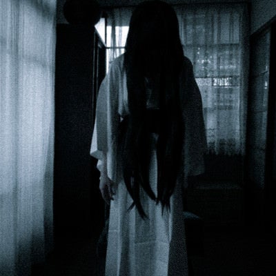 暗い室内でうつむく長髪の女の霊の写真