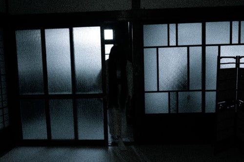 薄暗い部屋に入る黒髪長髪の女性の写真
