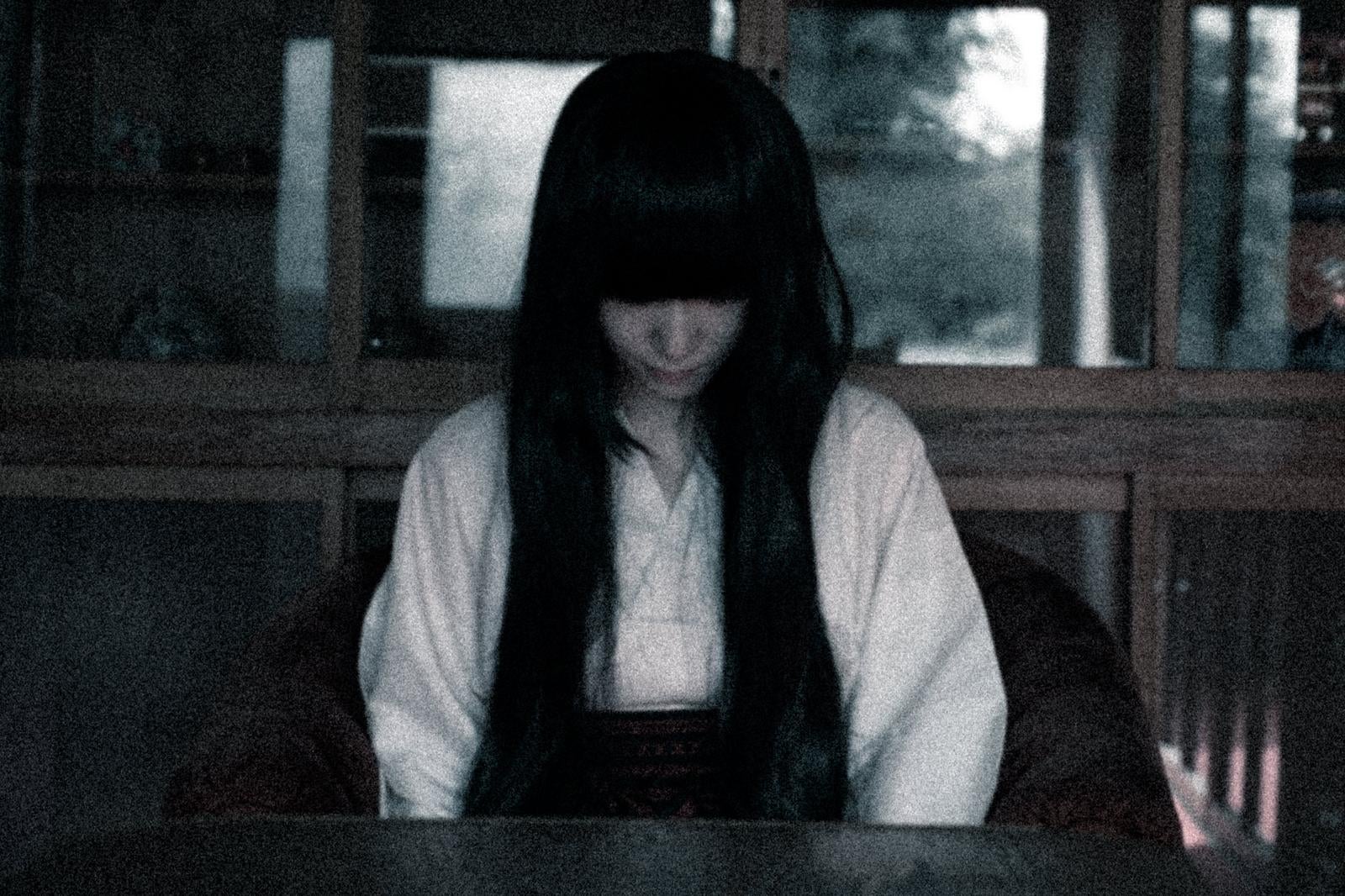 薄暗い室内で俯いている長い黒髪の女性［モデル：緋真煉］