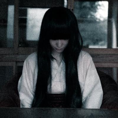薄暗い室内で俯く長い黒髪の女性の写真