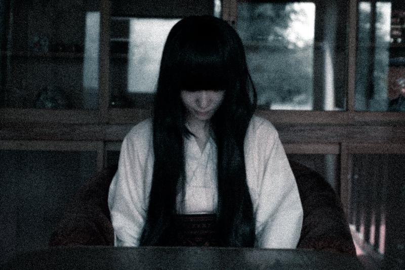 薄暗い室内で俯く長い黒髪の女性の写真