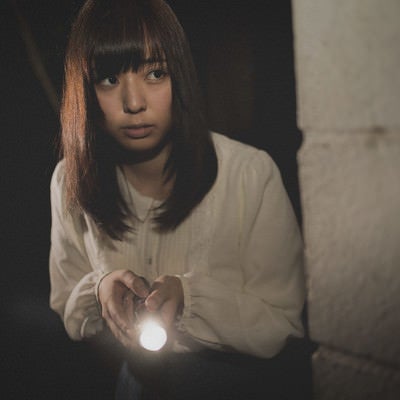 深夜にひとりで懐中電灯を持ち廃墟を探索する女性の写真