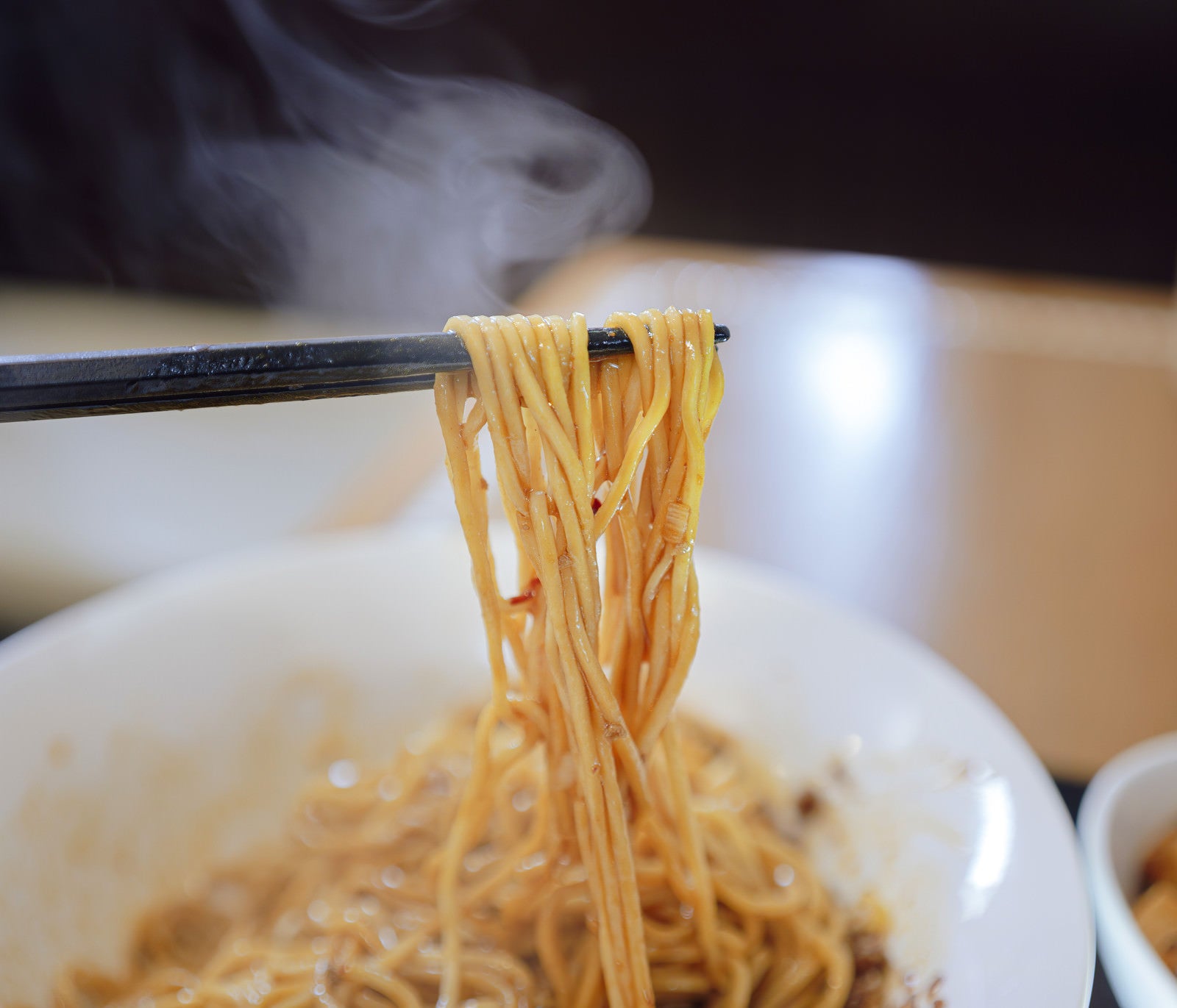 「熱々の汁なし担々麺を箸で持ち上げる」の写真