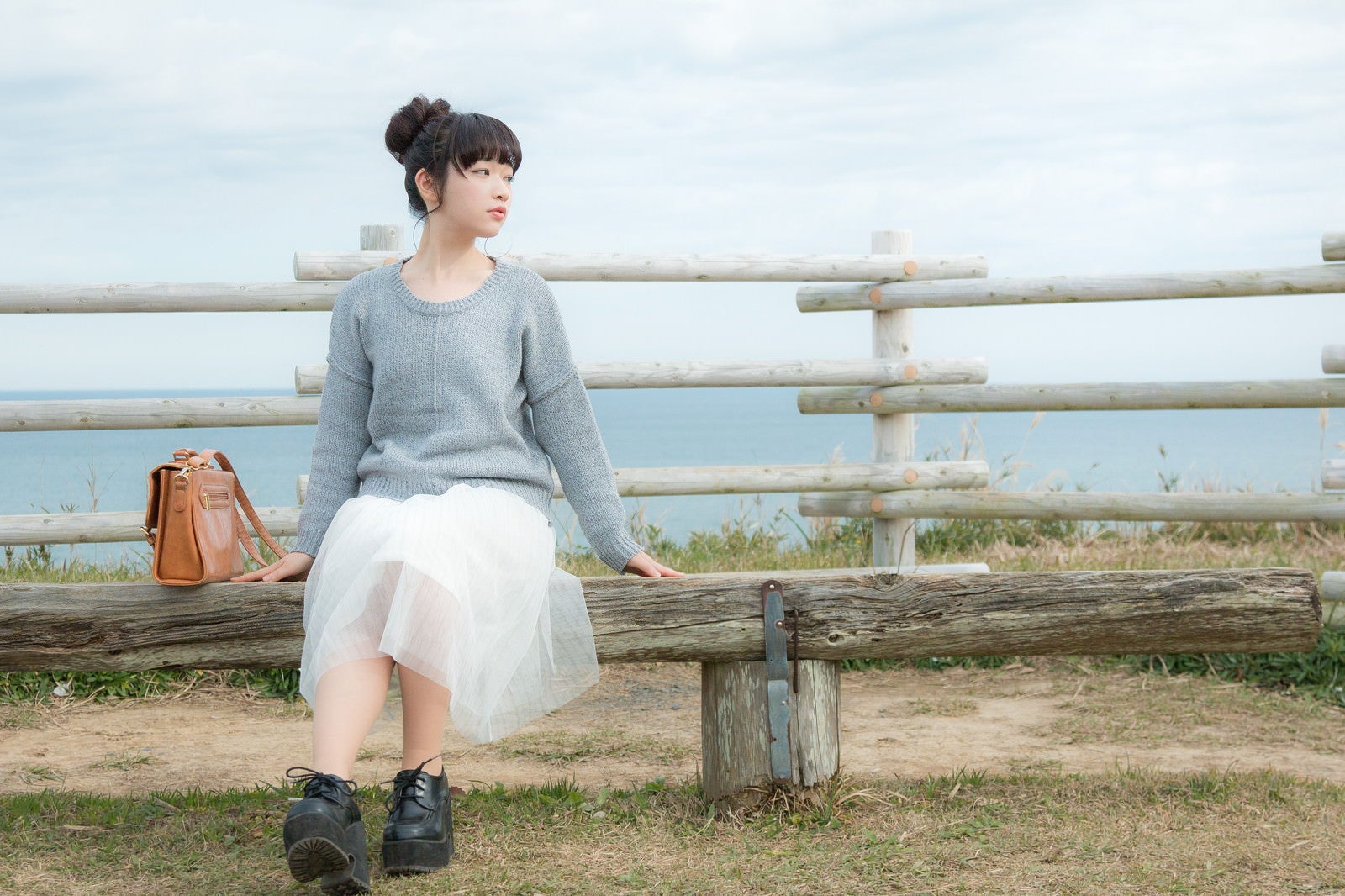 「海が一望できる岬のベンチに座る若い女性」の写真［モデル：渡辺友美子］