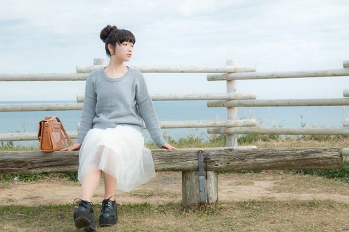 海が一望できる岬のベンチに座る若い女性の写真