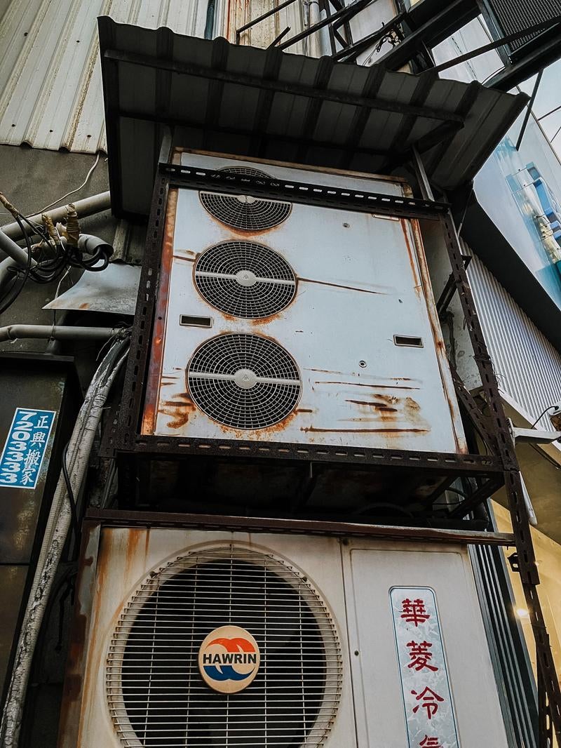 「老朽化したビルの壁に設置された業務用エアコンの室外機」の写真
