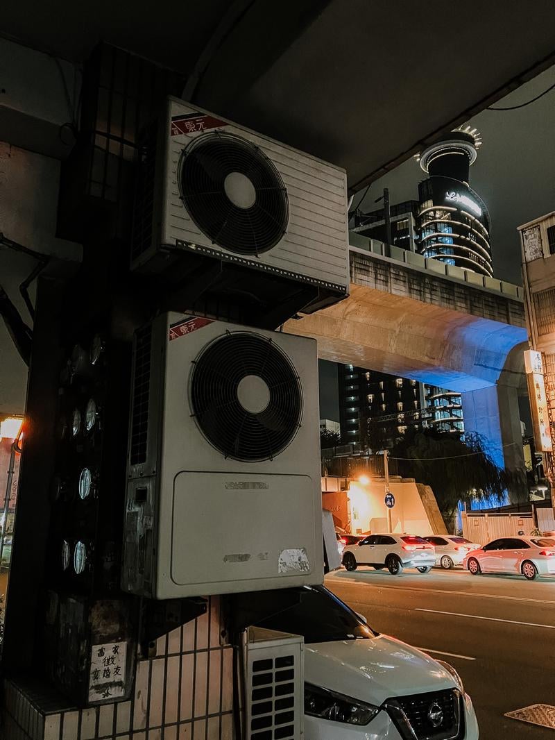 古びたエアコン室外機が並ぶ雑然としたビル裏路地の写真