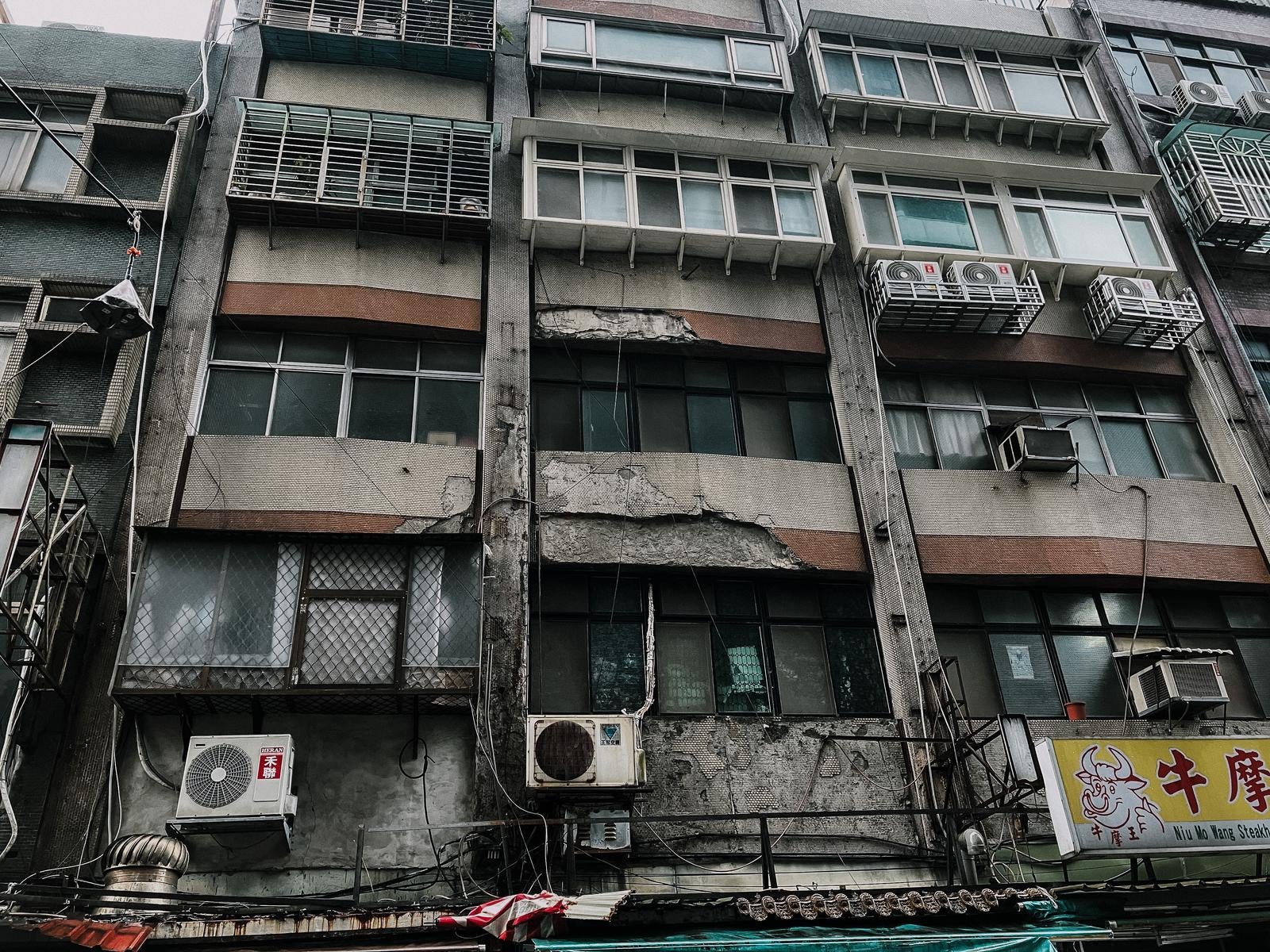 「老朽化したビルの外観とエアコンの室外機が並ぶ都市の一角」の写真