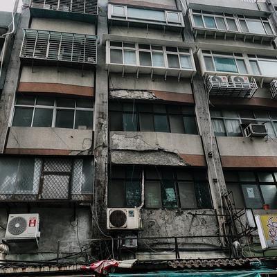 老朽化したビルの外観とエアコンの室外機が並ぶ都市の一角の写真