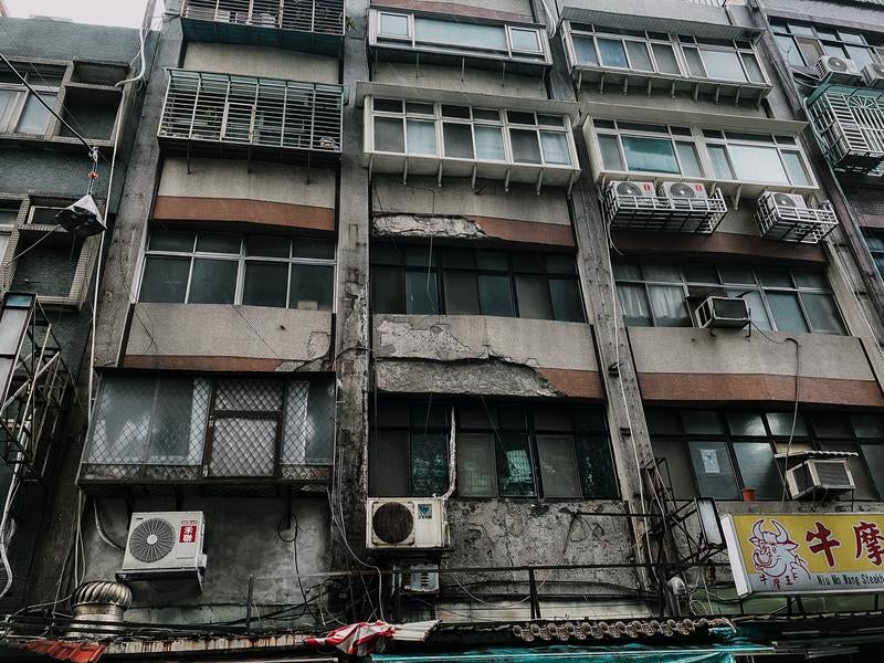 老朽化したビルの外観とエアコンの室外機が並ぶ都市の一角の写真