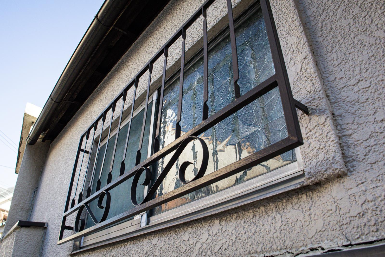 白い外壁の住宅にある小窓と、渦巻き模様の装飾が施された黒い鉄格子