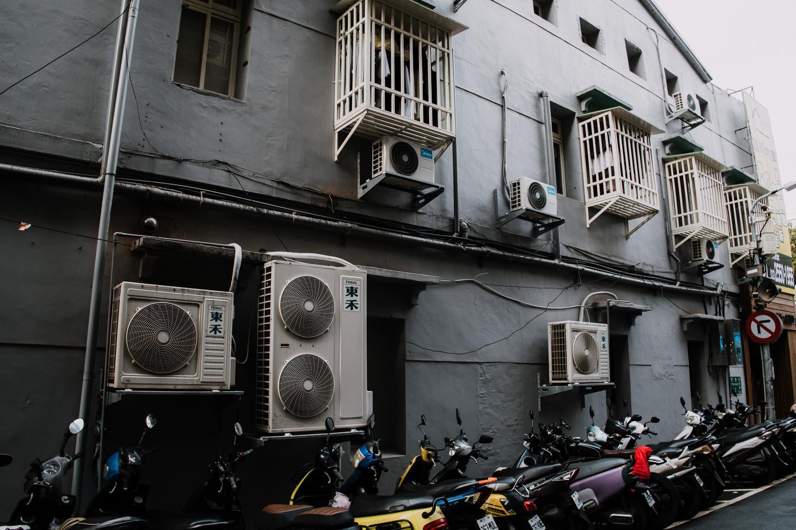 「バイクとエアコン室外機が並ぶ雑多な路地裏」の写真
