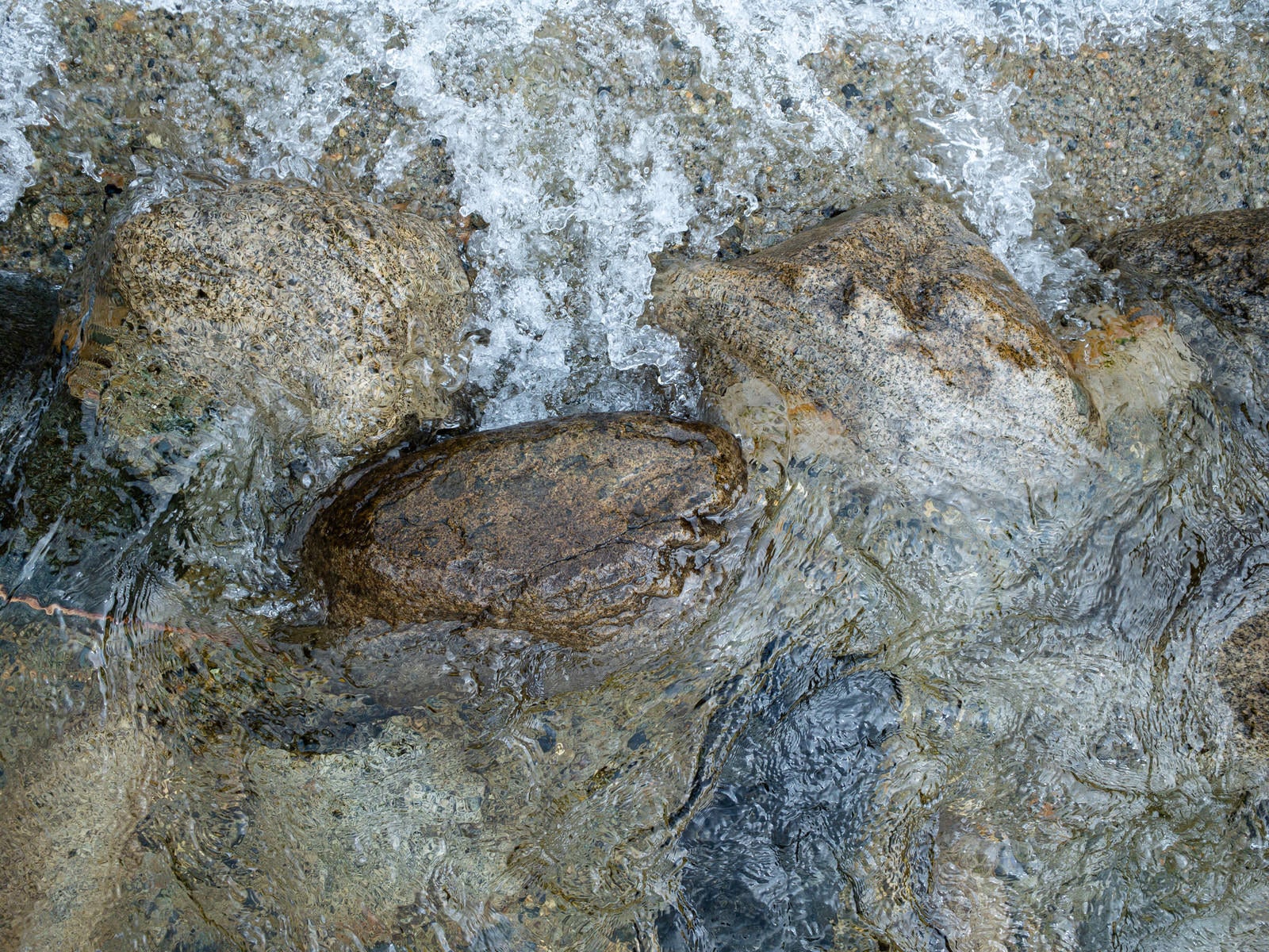 茶色や灰色の岩石の間を透明な水が流れている自然の風景