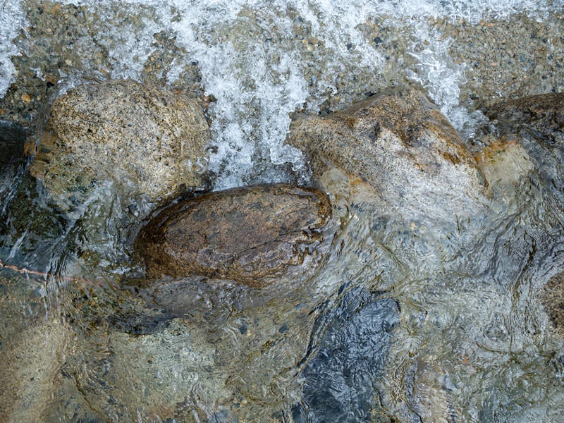 河原の石の間を流れる透明な水（テクスチャー）の写真