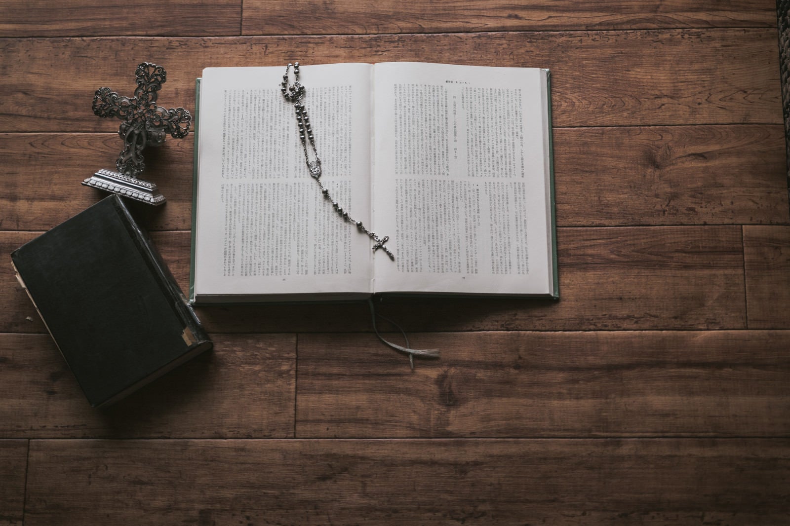「木目板の上に置かれた聖書とロザリオ」の写真