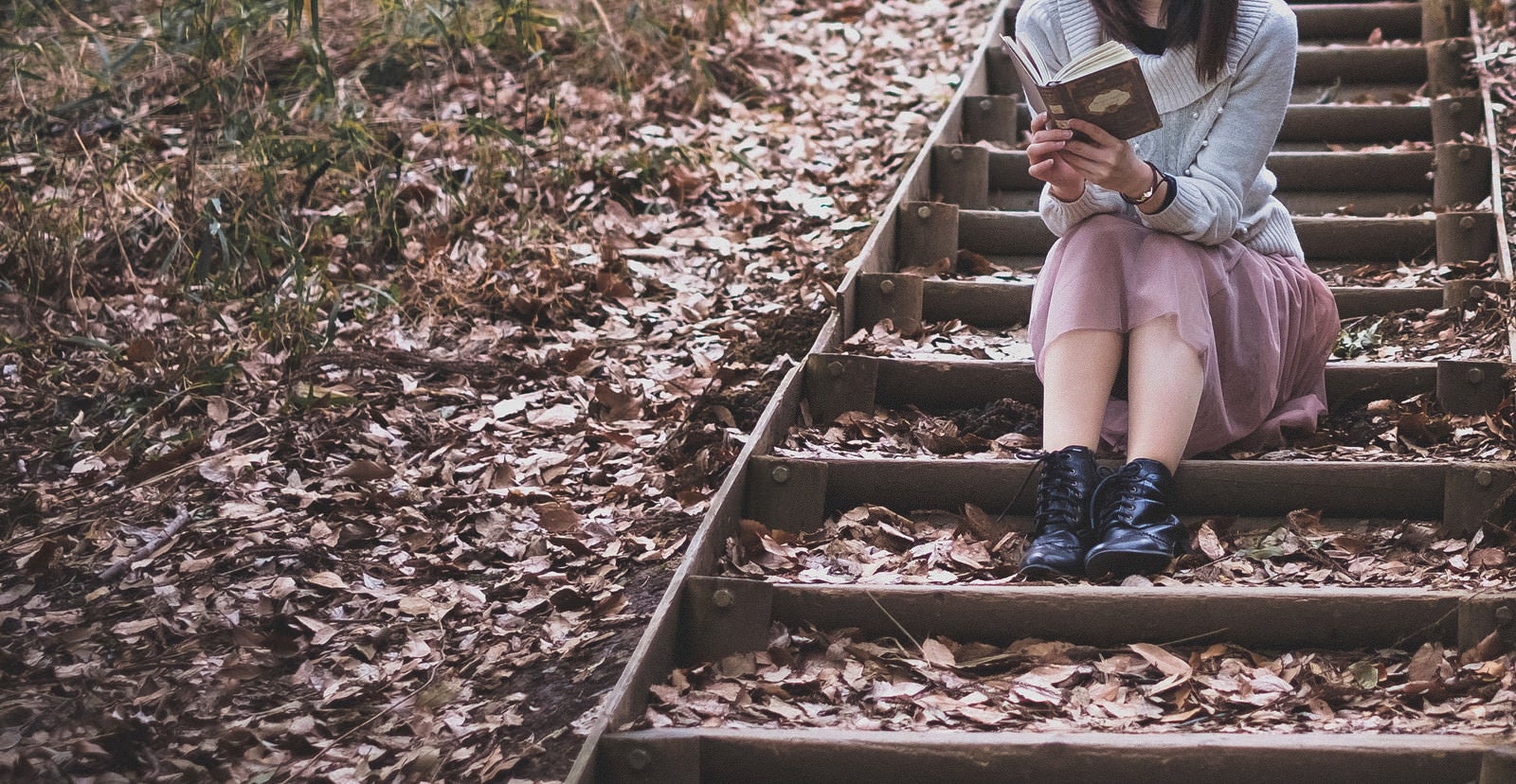 「落ち葉が積もる階段で読書に耽る女性」の写真