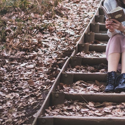 落ち葉が積もる階段で読書に耽る女性の写真