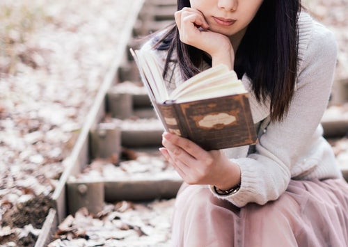 屋外で洋書を読む女性の写真