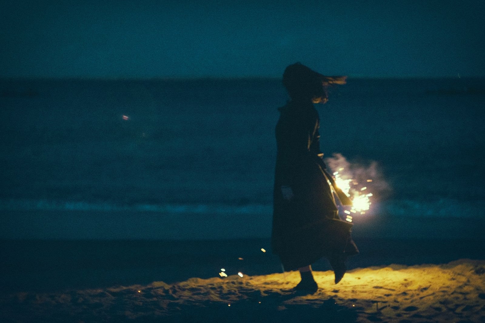 「夜の浜辺で手持ち花火と女性のシルエット」の写真