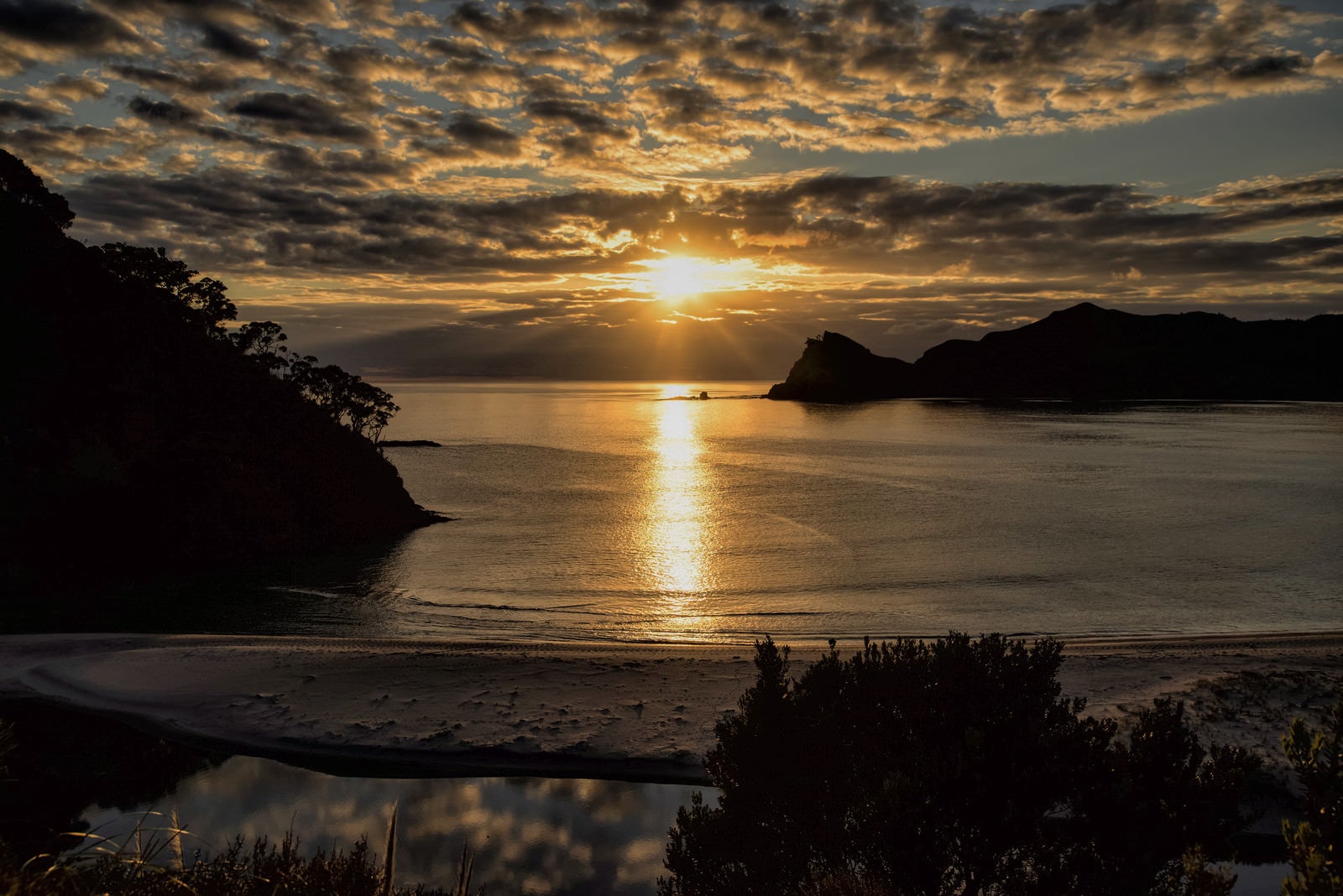 「グレートバリア島の浜辺まで延びるレイラインと朝日（ニュージーランド）」の写真