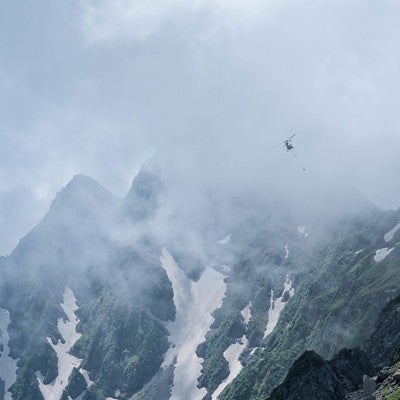 雲間を飛ぶ荷揚げのヘリコプター（穂高連峰）の写真