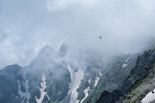 雲間を飛ぶ荷揚げのヘリコプター（穂高連峰）の写真
