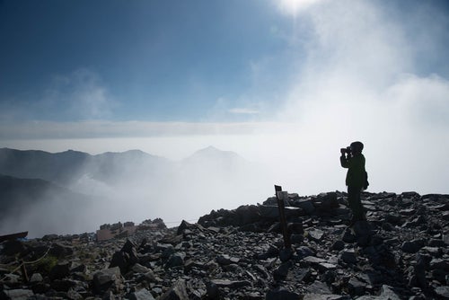 雲の上の北穂高岳山頂に立つ登山者（北アルプス）の写真