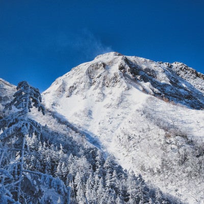 雪煙の上がる阿弥陀岳（八ヶ岳連峰）の写真