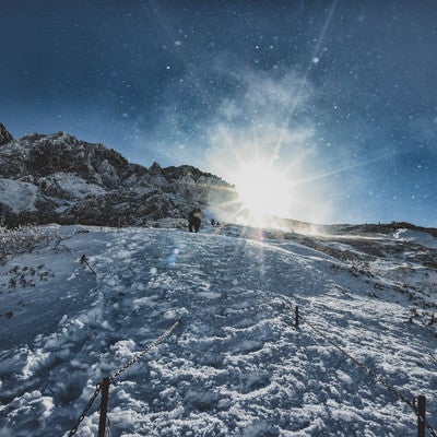 雪煙舞う稜線と登山者の写真