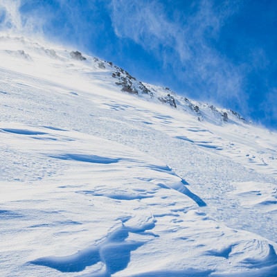 風吹き荒れる雪山の斜面の写真