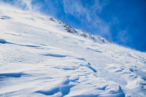 風吹き荒れる雪山の斜面の写真