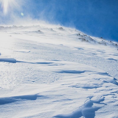 太陽を一面に浴びる雪山の斜面の写真