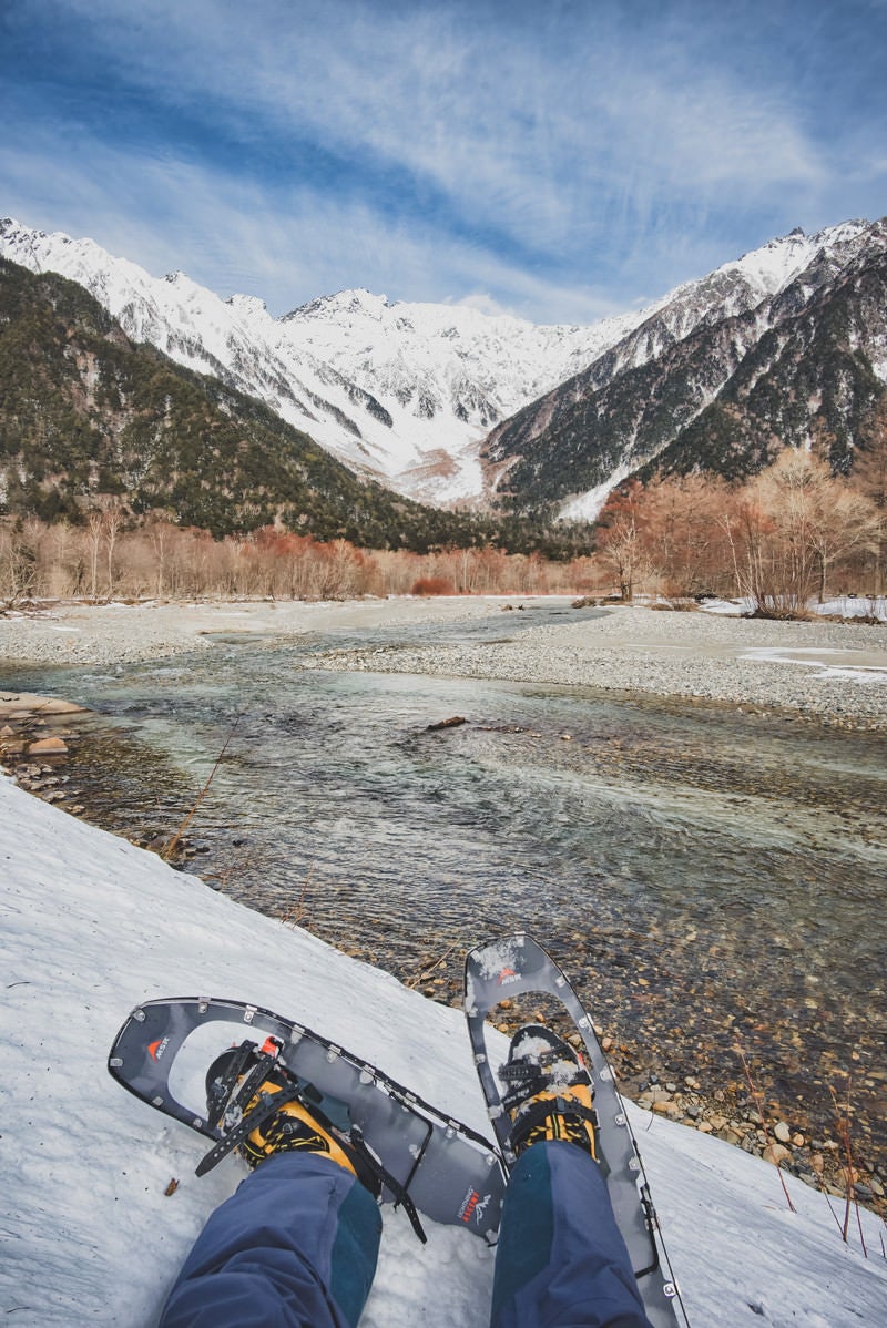 上高地から流れる川とスノートレッキング中の登山者の写真