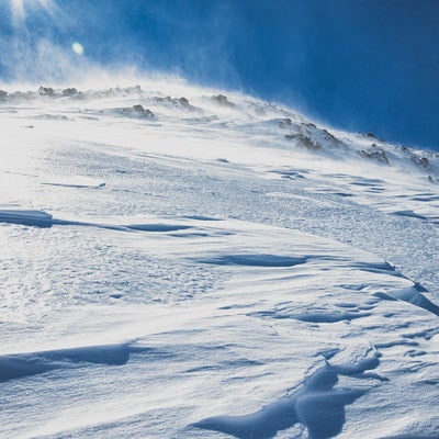 強風に晒される雪山の斜面の写真