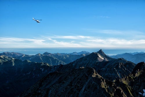 登山道から望む北アルプスとヘリコプターの写真