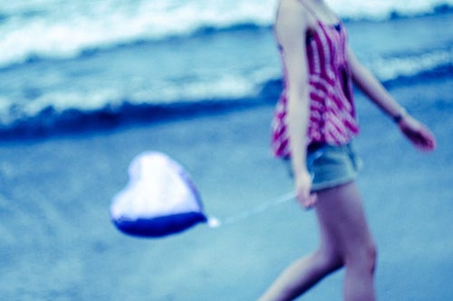 ハートを持って砂浜を歩く女性の写真