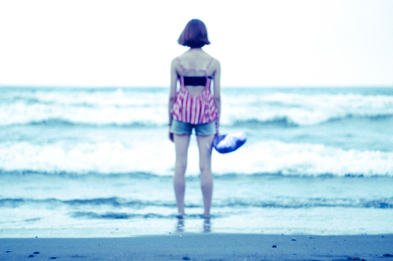 「波打ち際で海を眺める女性の後姿」の写真