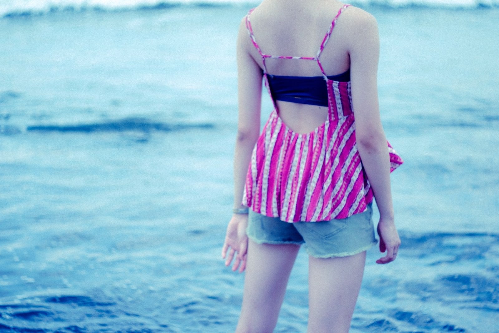 「波打ち際に立ちすくむ若い女性の後ろ姿（夏）」の写真