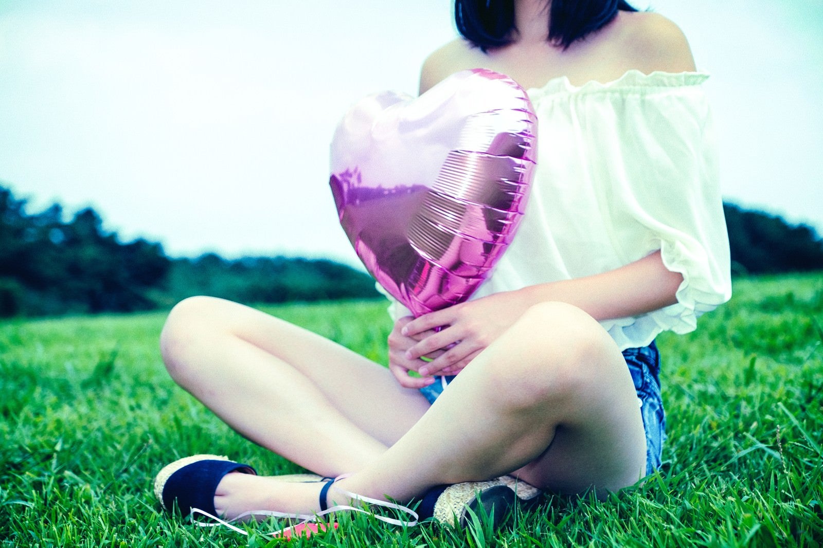 「芝生の上でハートの風船を持って座る女子」の写真