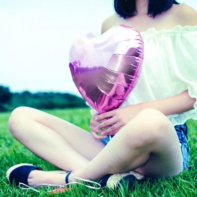 芝生の上でハートの風船を持って座る女子の写真