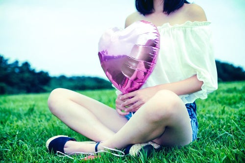 芝生の上でハートの風船を持って座る女子の写真
